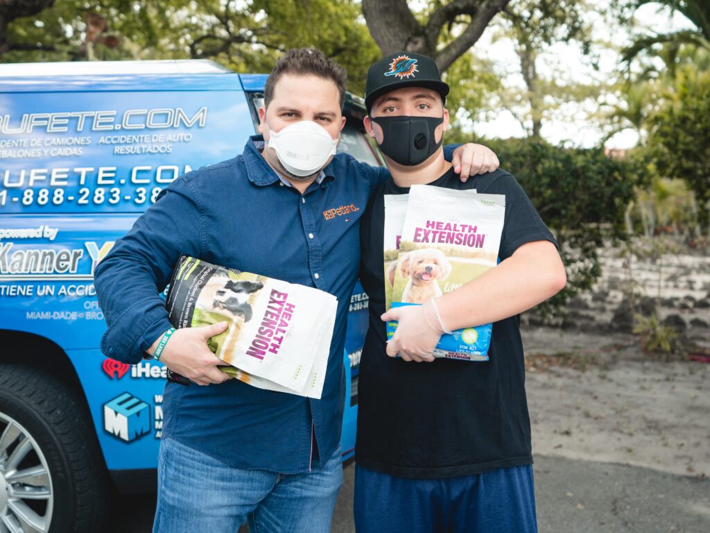 Petland Pembroke Pines picture of Petland owner, Luis Marquez and a pet owner holding bags of dog food and standing in front of a blue van.
